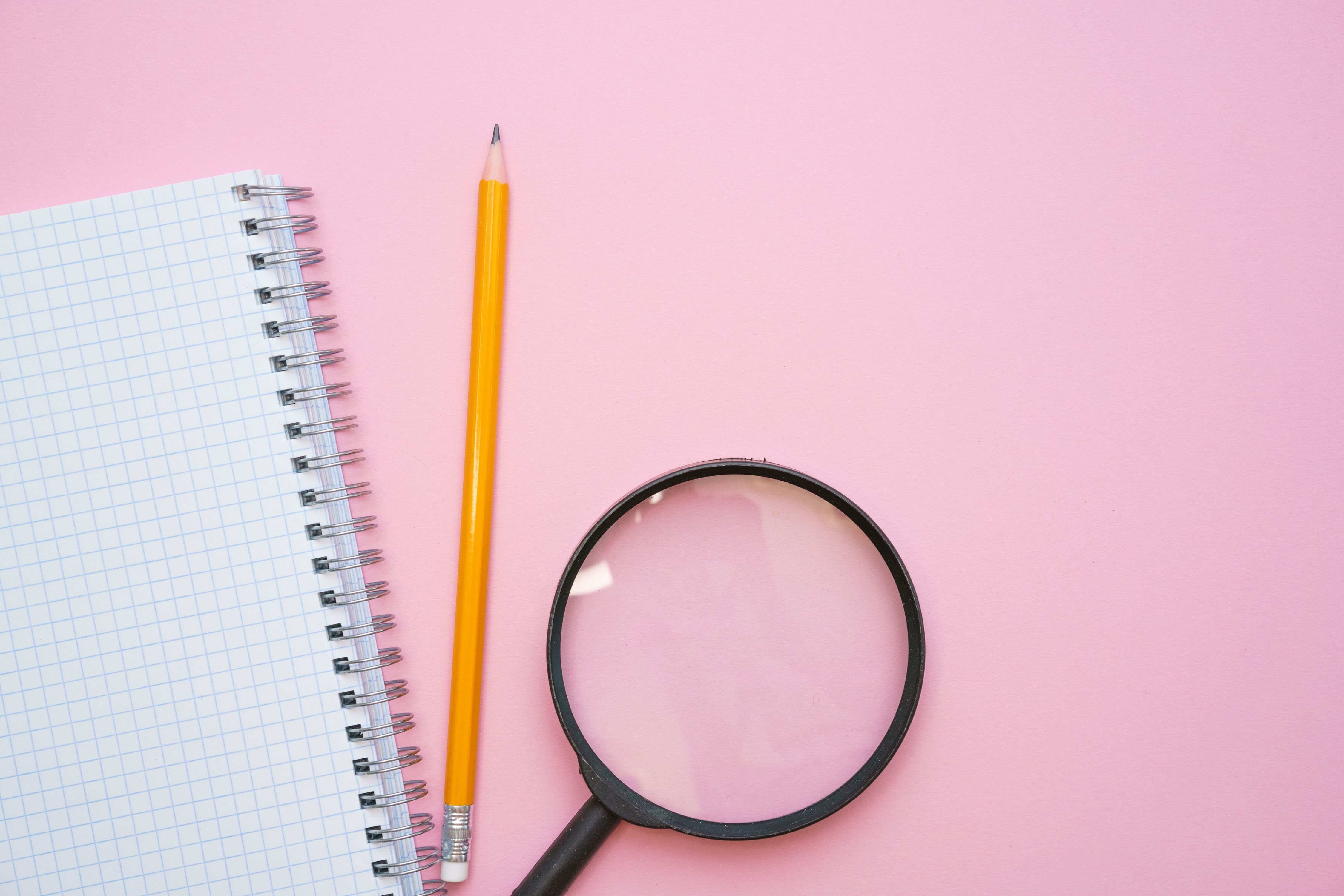 A magnifying glass, a pencil, and a notebook for performing amazon keyword research