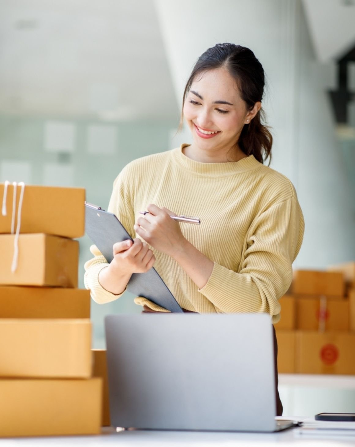 woman working at a desk with a laptop surrounded by cardboard boxes