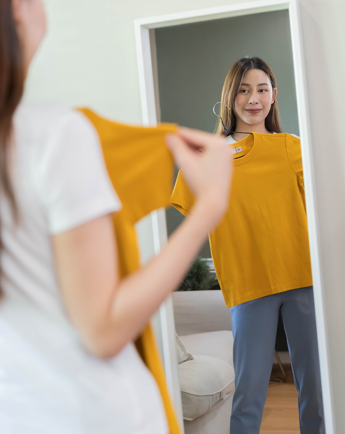 woman holding yellow t-shirt in front of mirror