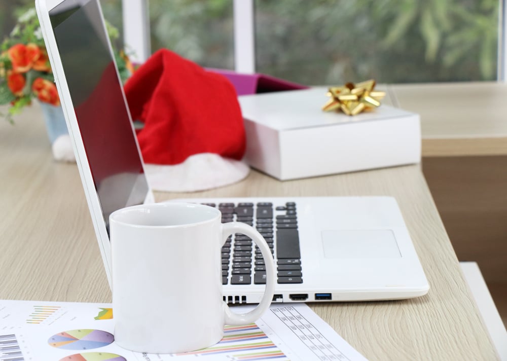 desk with laptop, box with a bow, mug, and a santa hat