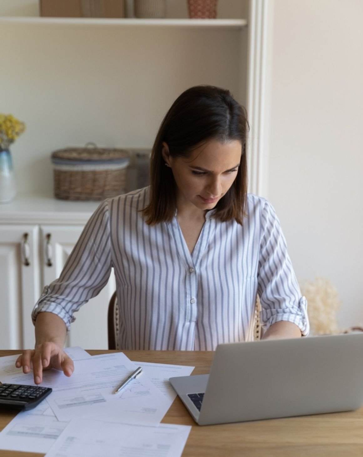 woman sitting at a desk focused on her laptop with scattered papers